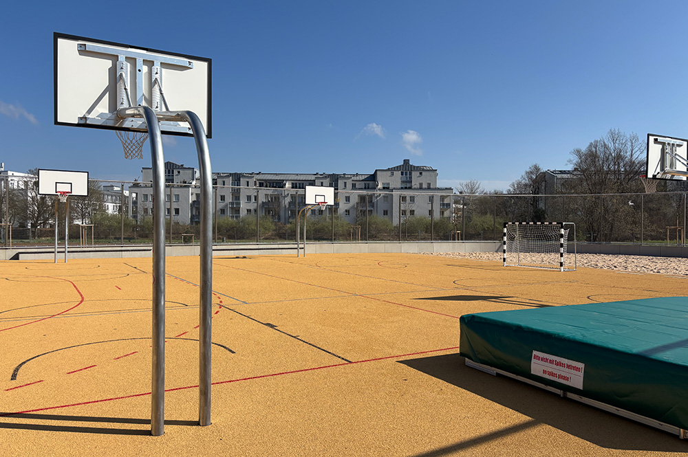 Basketballständer auf Sportplatz, rechts Hochsprungmatte